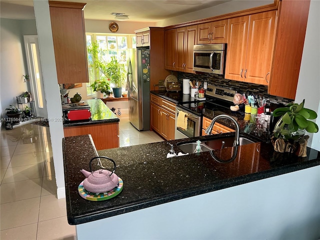 kitchen featuring light tile patterned floors, a sink, appliances with stainless steel finishes, tasteful backsplash, and brown cabinetry