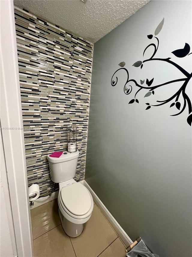 bathroom featuring tile walls, toilet, a textured ceiling, tile patterned flooring, and baseboards