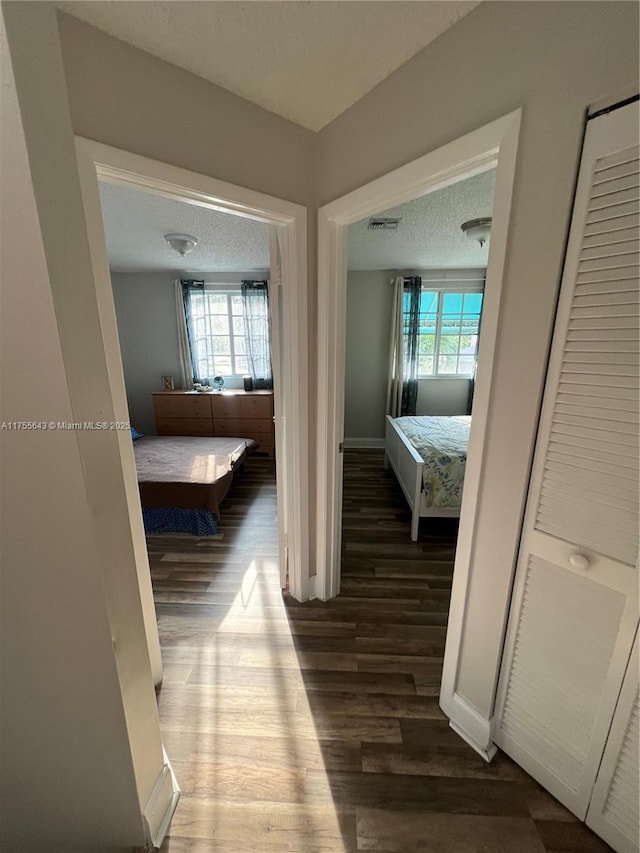 hallway with visible vents, a textured ceiling, baseboards, and wood finished floors