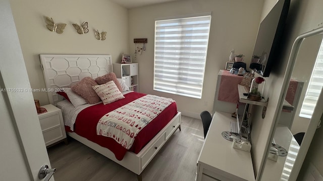 bedroom with multiple windows, wood finished floors, and baseboards