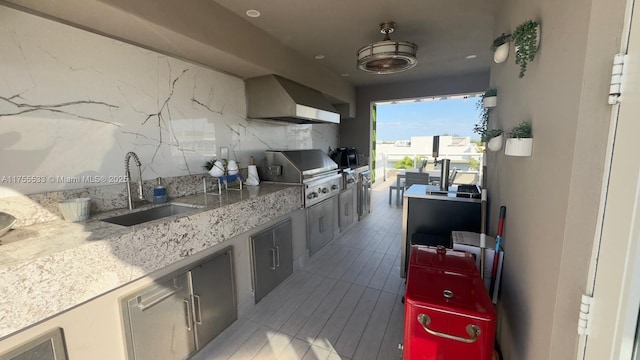 kitchen featuring wall chimney range hood, backsplash, a sink, and light stone counters