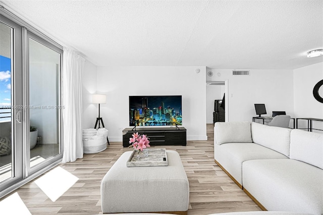 living room featuring visible vents, a textured ceiling, baseboards, and light wood-type flooring