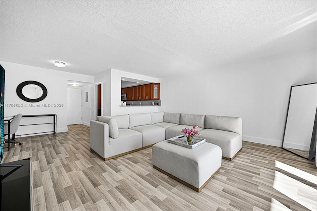 living area featuring a textured ceiling, baseboards, and light wood-type flooring