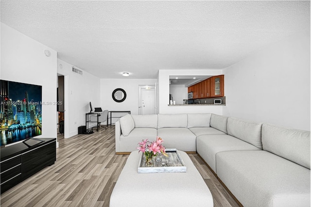 living area with baseboards, a textured ceiling, visible vents, and light wood-style flooring