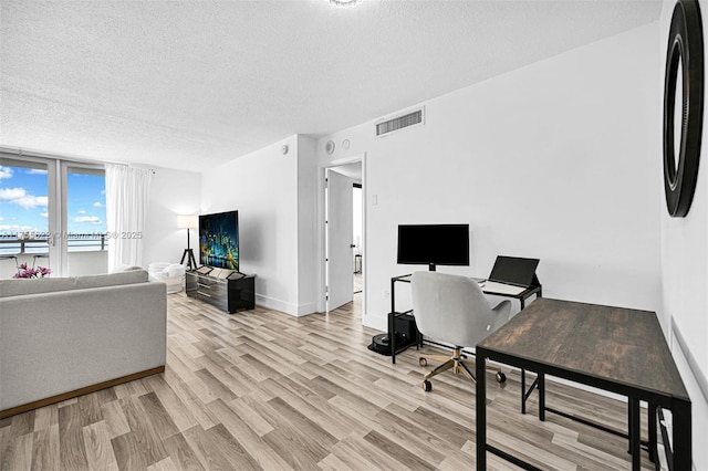 office space with a textured ceiling, baseboards, light wood-style flooring, and visible vents