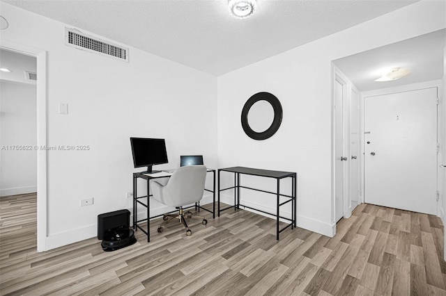 office with baseboards, a textured ceiling, wood finished floors, and visible vents