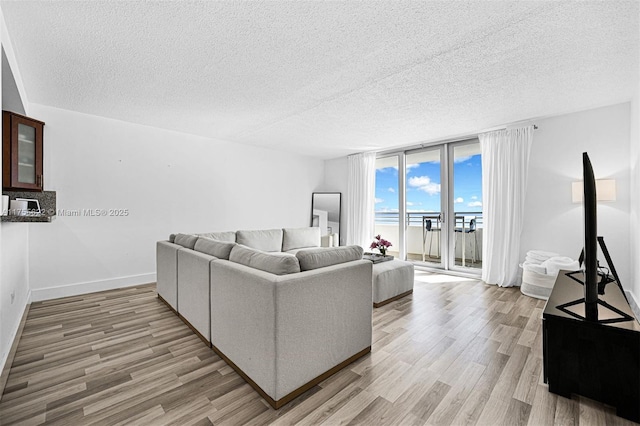 living room with baseboards, a textured ceiling, and light wood-style flooring