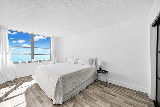 bedroom with baseboards, a water view, a textured ceiling, and wood finished floors