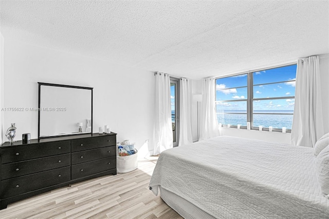 bedroom with a water view, a textured ceiling, and wood finished floors