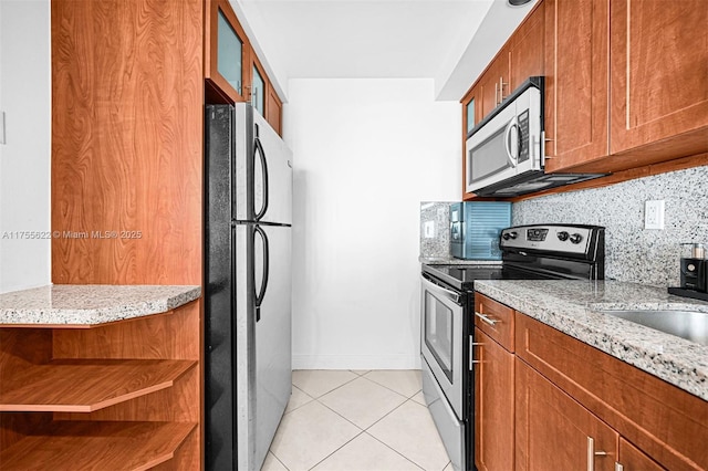 kitchen with light tile patterned floors, appliances with stainless steel finishes, brown cabinets, and light stone counters