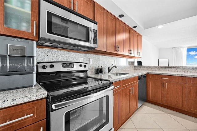 kitchen featuring brown cabinets, stainless steel appliances, light stone countertops, and a sink