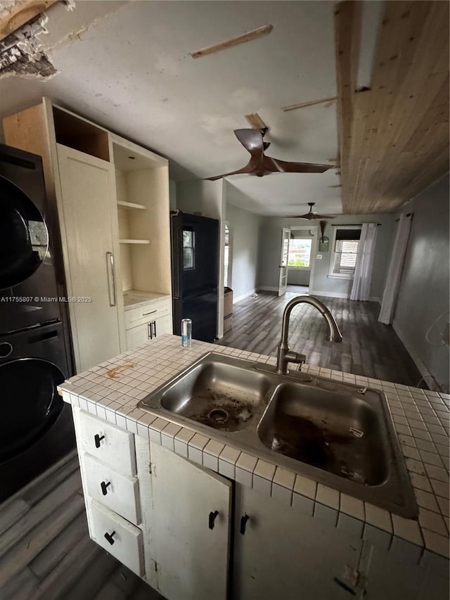 kitchen with tile countertops, a sink, white cabinetry, stacked washing maching and dryer, and freestanding refrigerator