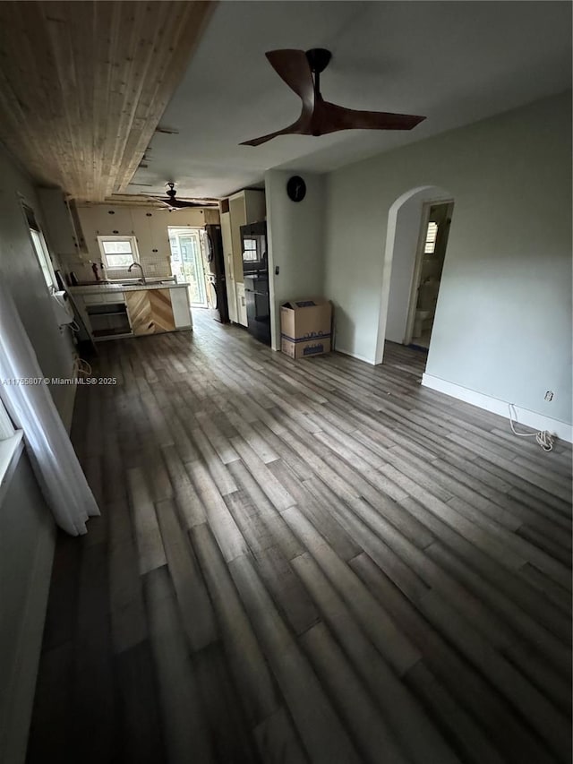 unfurnished living room with a ceiling fan, baseboards, arched walkways, and dark wood-style flooring