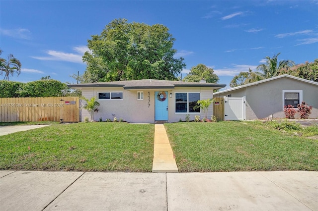 ranch-style home featuring a front lawn, fence, a gate, and stucco siding