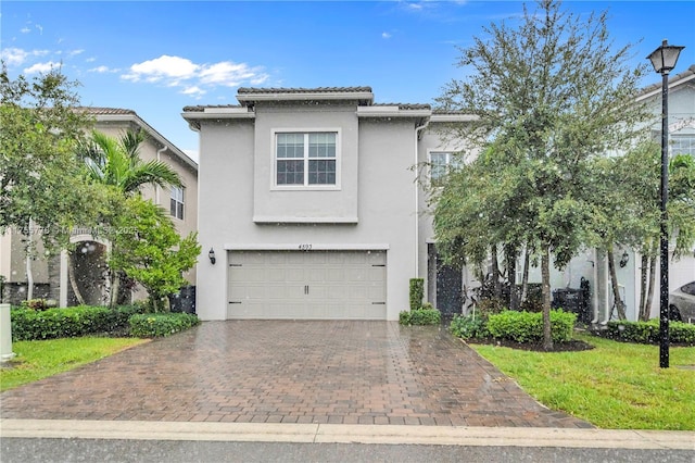 view of front of house featuring decorative driveway, stucco siding, an attached garage, a front yard, and a tiled roof