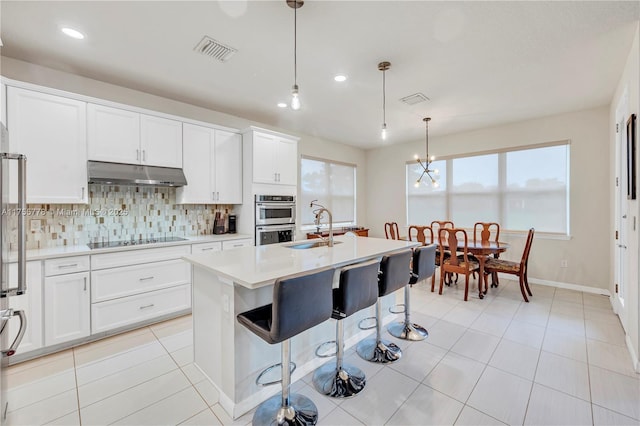 kitchen featuring black electric stovetop, under cabinet range hood, a sink, visible vents, and backsplash