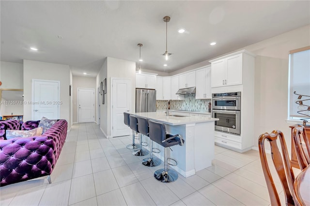 kitchen with a breakfast bar area, under cabinet range hood, light countertops, appliances with stainless steel finishes, and backsplash