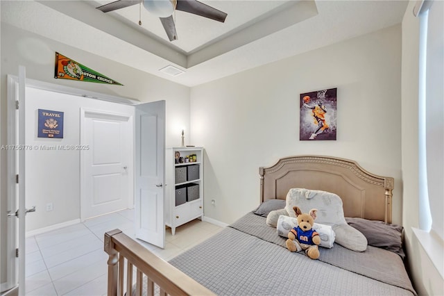 bedroom with light tile patterned floors, ceiling fan, a tray ceiling, and baseboards