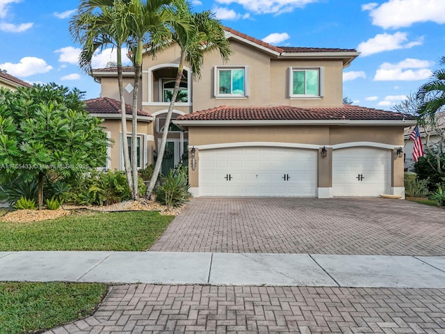 mediterranean / spanish house with a garage, decorative driveway, a tile roof, and stucco siding