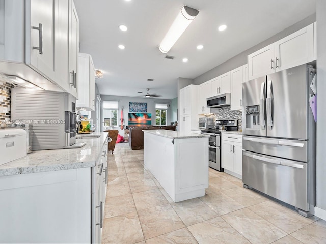 kitchen with a ceiling fan, white cabinets, open floor plan, appliances with stainless steel finishes, and tasteful backsplash