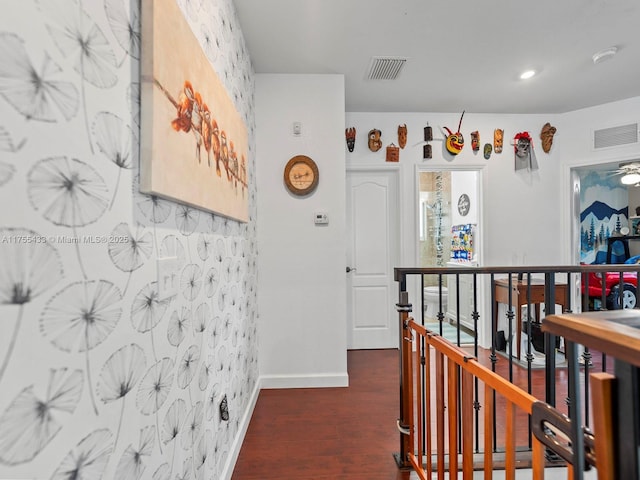 hallway featuring dark wood-type flooring, an upstairs landing, visible vents, and baseboards