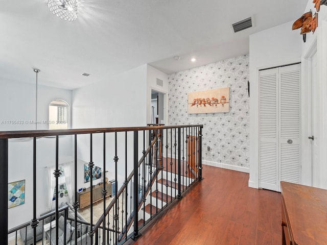 hall featuring visible vents, an upstairs landing, wood finished floors, baseboards, and wallpapered walls