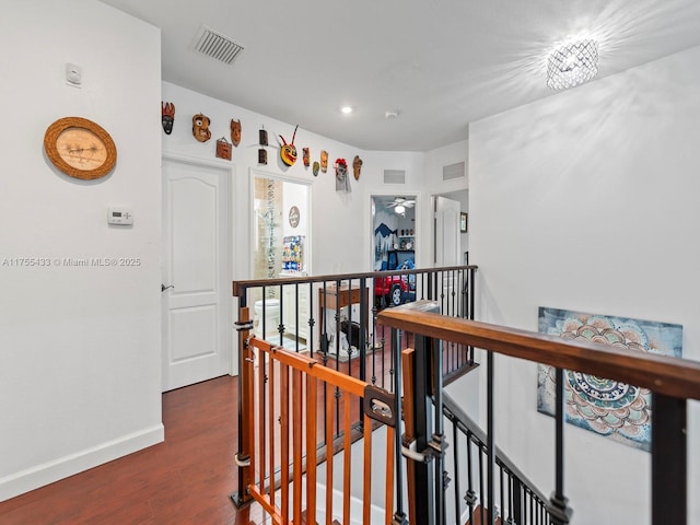 hall featuring baseboards, visible vents, dark wood finished floors, and an upstairs landing