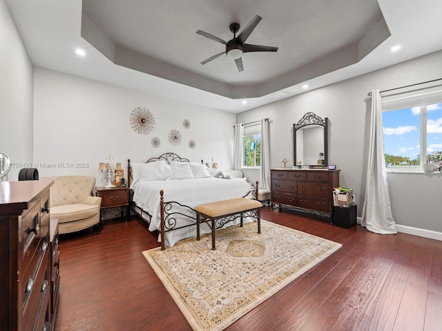 bedroom with dark wood-style floors, baseboards, a tray ceiling, and recessed lighting