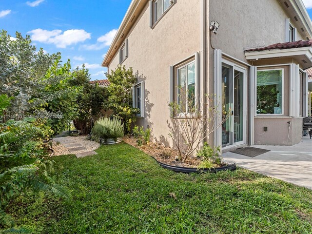 view of side of property with a yard, a patio area, a tile roof, and stucco siding