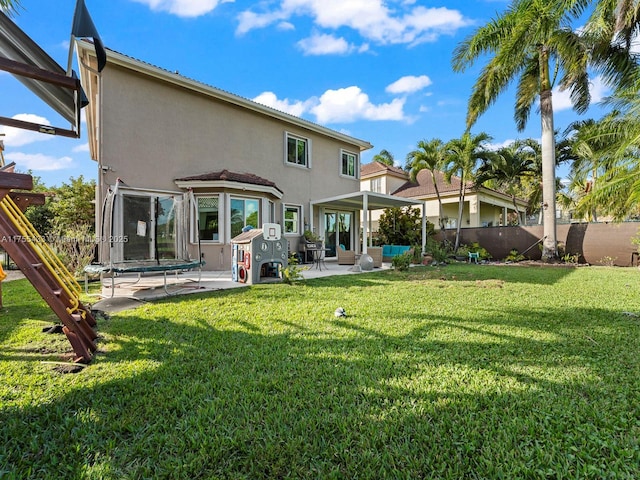 rear view of property with fence, a lawn, stucco siding, a trampoline, and a patio area