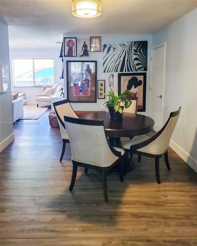 dining room featuring a textured ceiling, wood finished floors, and baseboards