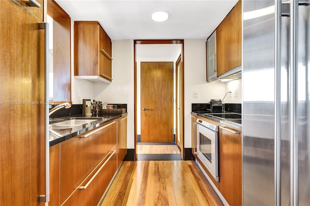 kitchen with high end fridge, brown cabinetry, a sink, modern cabinets, and oven