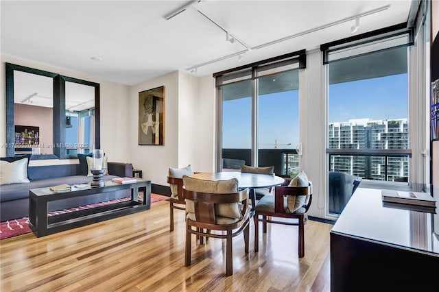 dining space featuring expansive windows, rail lighting, light wood finished floors, and a view of city