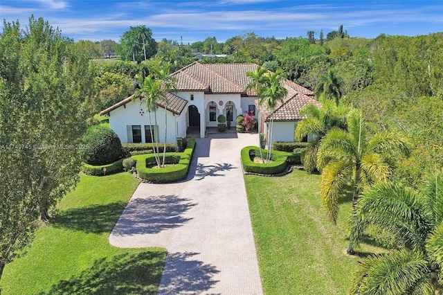 mediterranean / spanish house with decorative driveway, a tile roof, a front lawn, and stucco siding