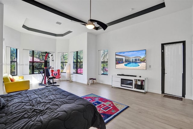 bedroom featuring baseboards, visible vents, a raised ceiling, a towering ceiling, and wood finished floors