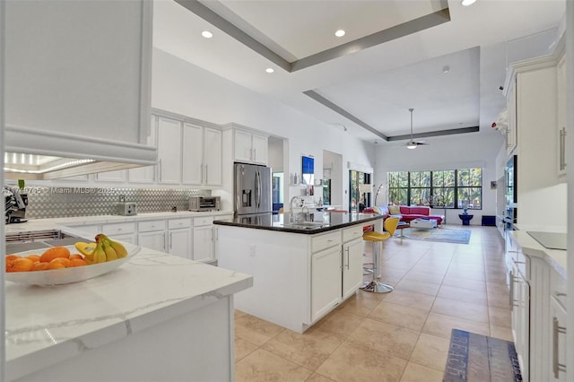 kitchen with stainless steel refrigerator with ice dispenser, a raised ceiling, backsplash, open floor plan, and a kitchen island