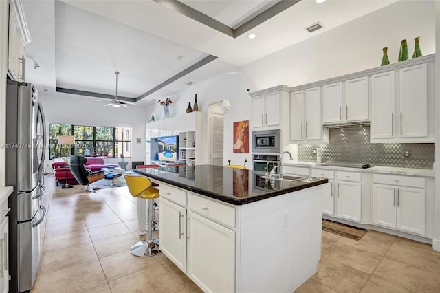 kitchen with a tray ceiling, visible vents, appliances with stainless steel finishes, open floor plan, and a sink