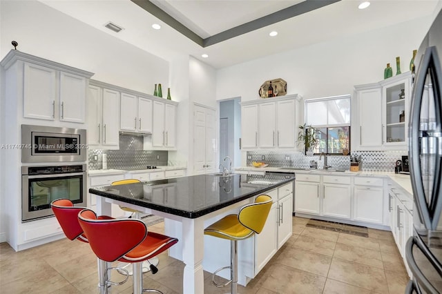 kitchen with stainless steel appliances, visible vents, backsplash, a sink, and a kitchen breakfast bar