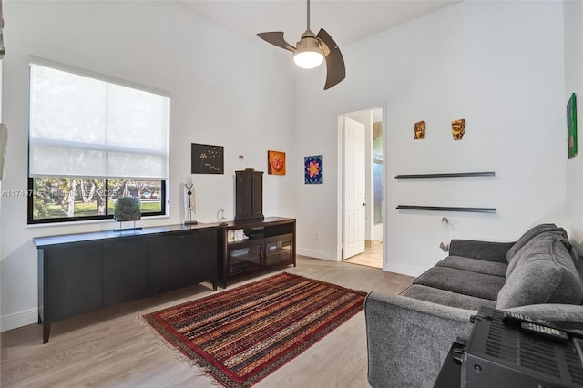 living room featuring a high ceiling, baseboards, ceiling fan, and light wood finished floors