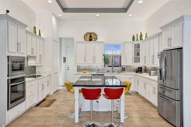 kitchen with appliances with stainless steel finishes, a tray ceiling, a sink, and light tile patterned floors