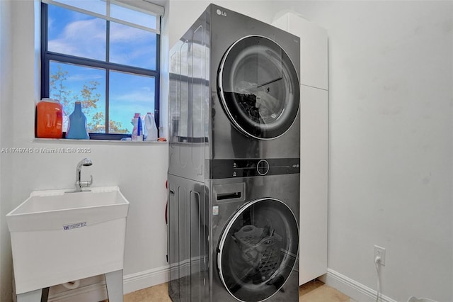 laundry room featuring baseboards, laundry area, a sink, and stacked washer / drying machine