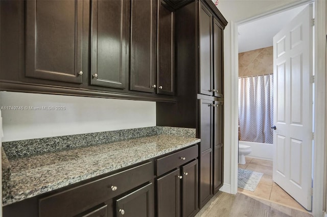 kitchen featuring light tile patterned flooring, dark brown cabinetry, and light stone countertops