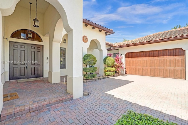 entrance to property featuring an attached garage, a tiled roof, and stucco siding