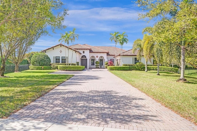 mediterranean / spanish home with decorative driveway, a front yard, a tile roof, and stucco siding