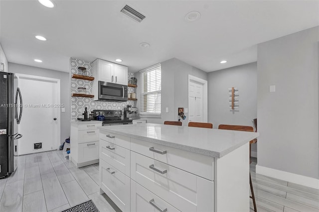 kitchen featuring a breakfast bar area, open shelves, stainless steel appliances, visible vents, and decorative backsplash