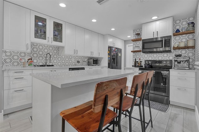 kitchen with a breakfast bar area, open shelves, stainless steel appliances, glass insert cabinets, and white cabinets