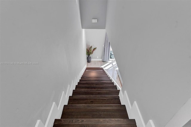 stairway featuring baseboards, a high ceiling, and wood finished floors