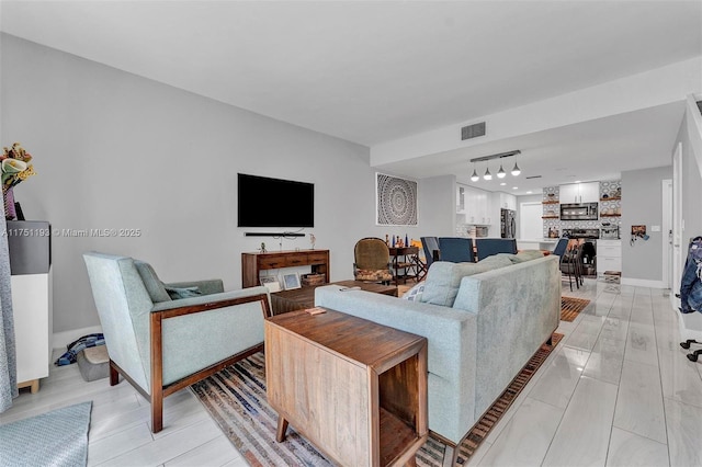 living room featuring light wood-type flooring, baseboards, visible vents, and track lighting