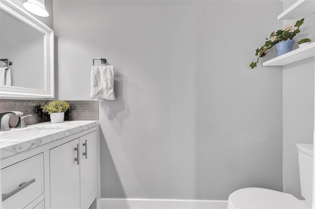 bathroom featuring toilet, baseboards, decorative backsplash, and vanity