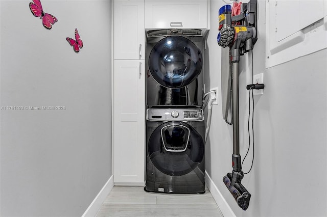 laundry area with stacked washer and dryer, cabinet space, light wood-style floors, and baseboards